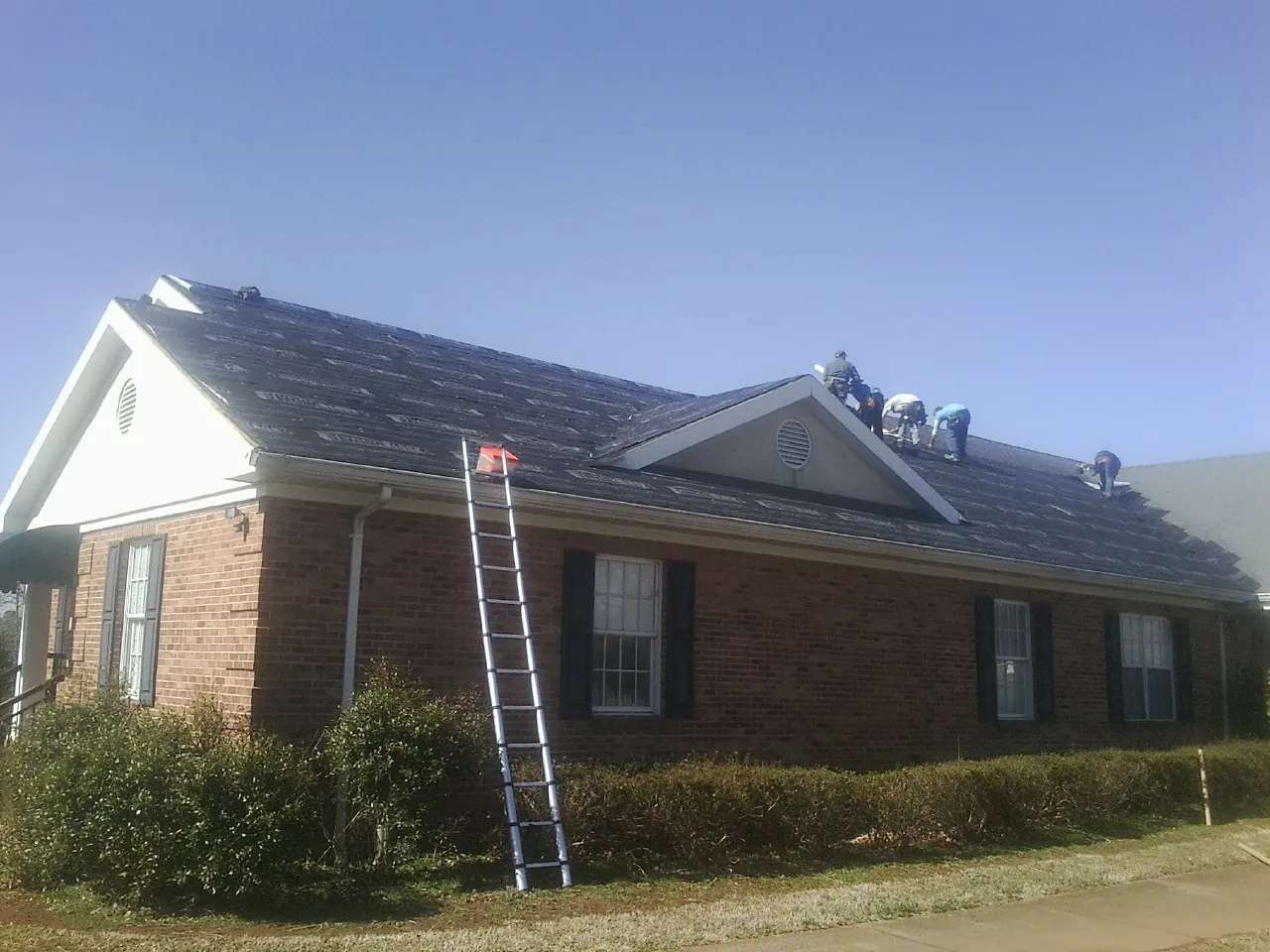 Crew tearing shingles off a brick ranch roof with a ladder set — Metal Roof Repair work by our crew in Rocky Hill