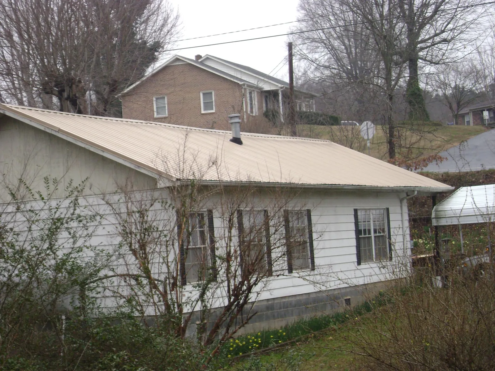 Tan metal roof on a white sided house set into a hillside — Commercial Roofing by Roofing Brothers in Rocky Hill